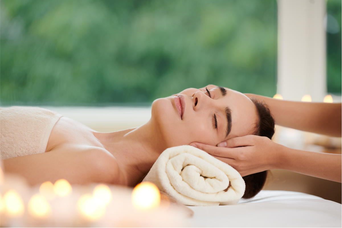 calm woman laying down on folded towel and getting her head massaged