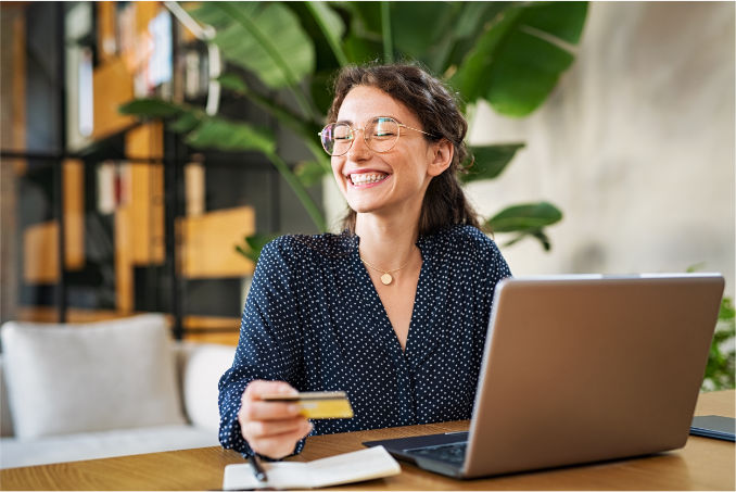 Smiling woman with glasses making an online booking on her laptop whilst holding a credit
card